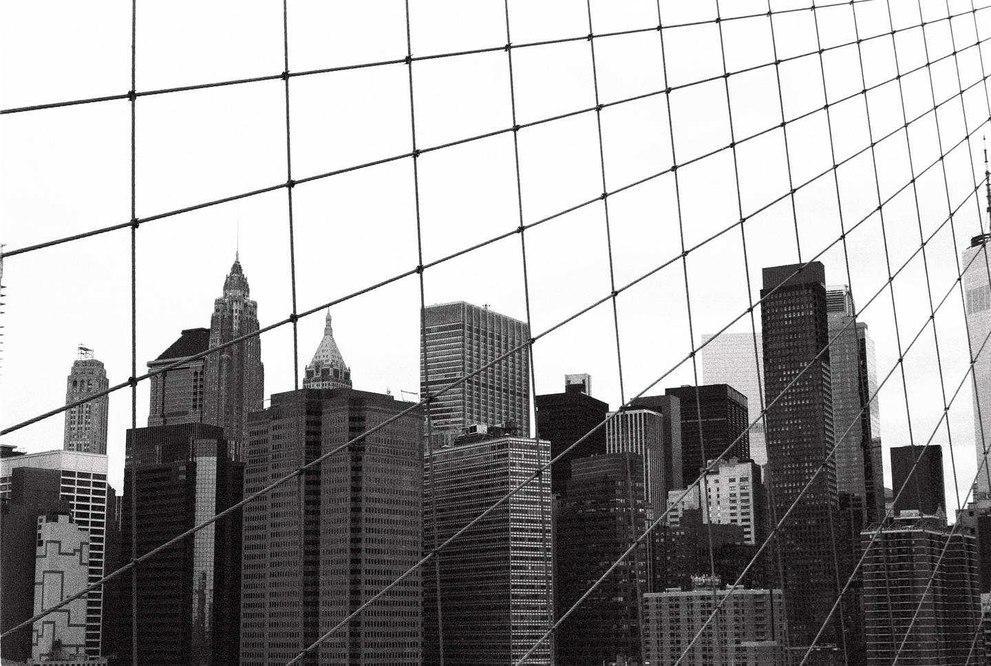A grid of wires from the Brooklyn Bridge frames a view of the New York City skyline.