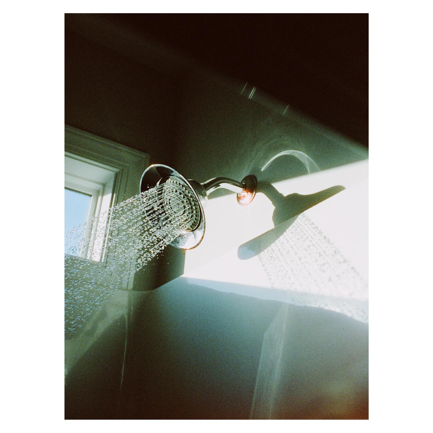 A shower head sprays water into a bathtub, illuminated by a shaft of sunlight.