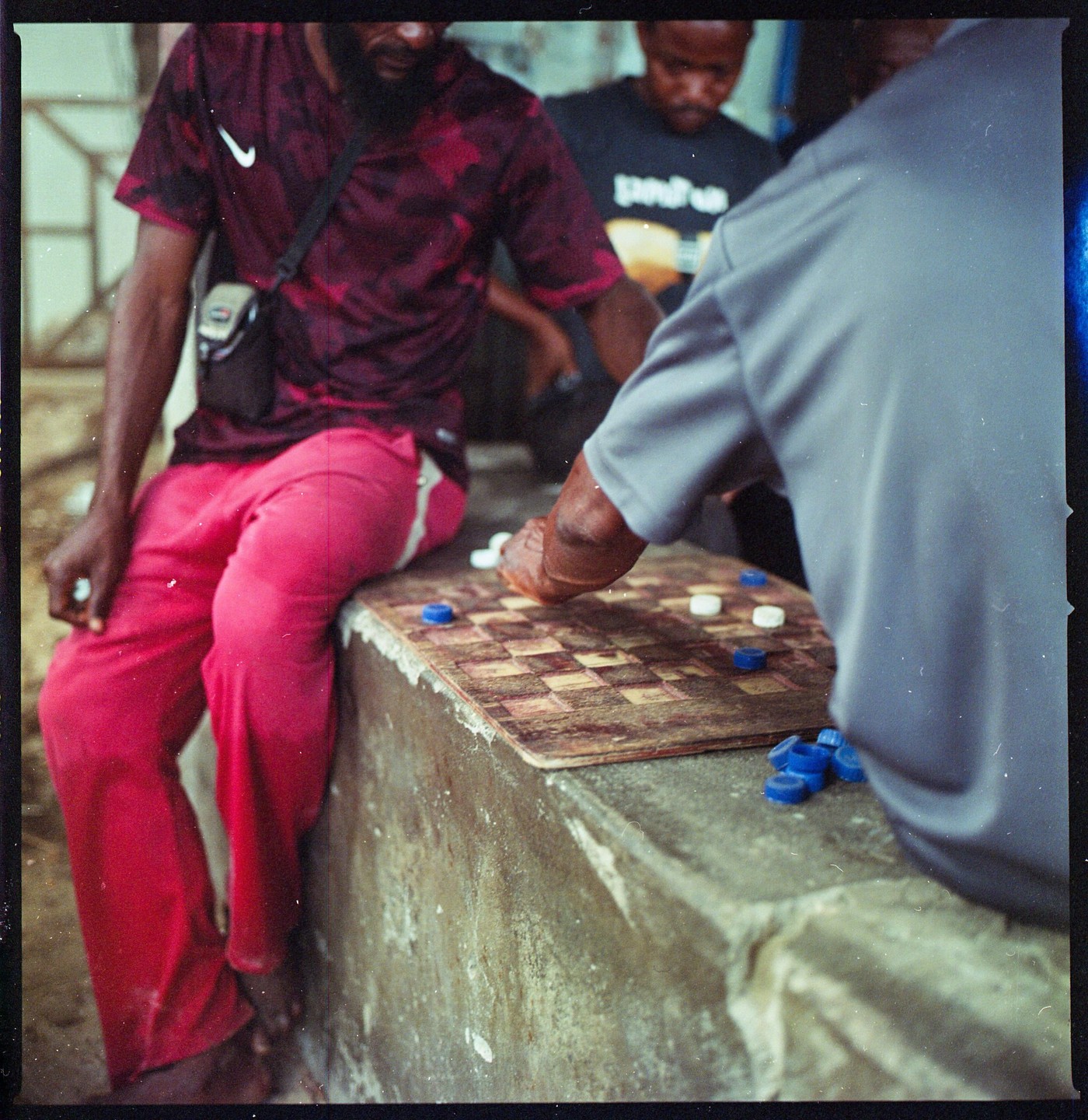 Three men play checkers on a concrete surface in Zanzibar.