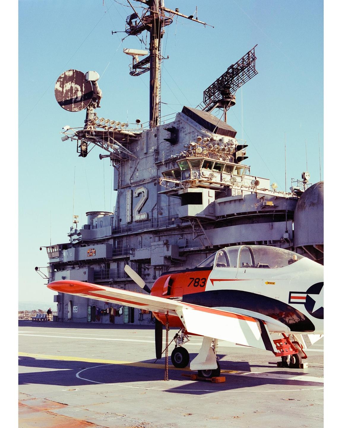 A small propeller plane is parked on the deck of a large aircraft carrier.