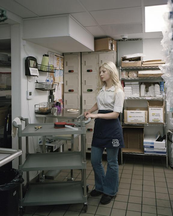 A woman stands next to a utility cart in a commercial kitchen.
