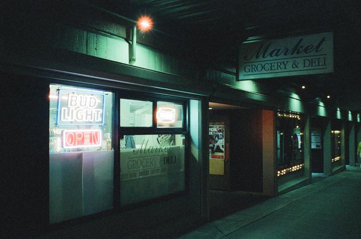 A grocery and deli storefront with neon signs is visible at night.