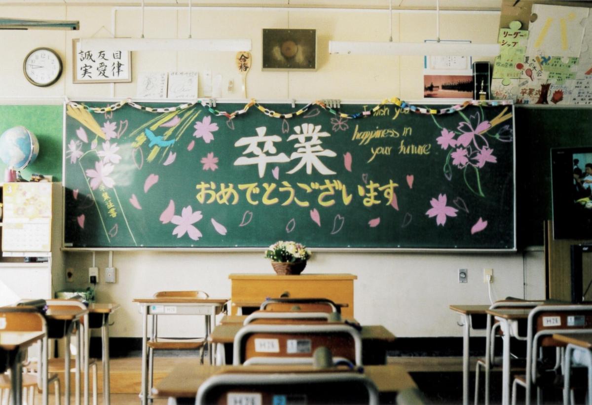 A classroom with rows of desks faces a chalkboard decorated with cherry blossoms and Japanese writing.
