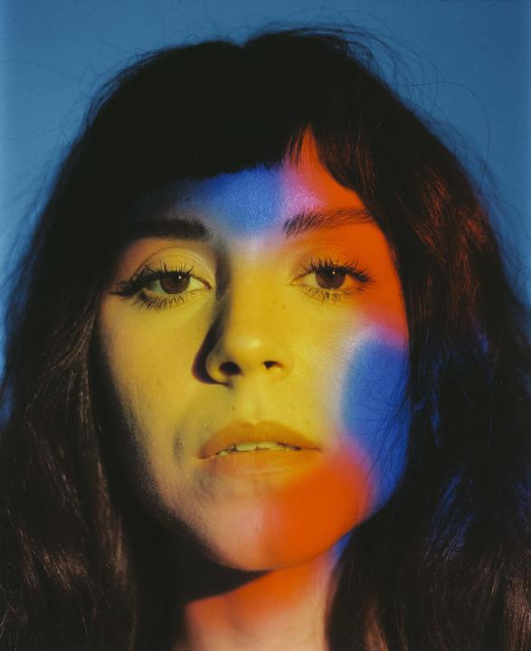 A woman's face is illuminated by blue, yellow, and red light.