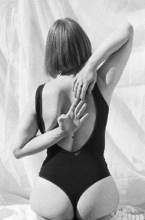 A woman in a swimsuit is kneeling with her hands clasped behind her back.