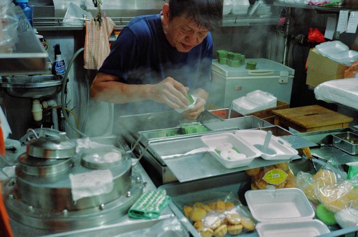 A man prepares food in a steamy kitchen filled with various containers and cooking equipment.