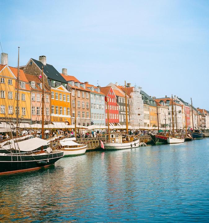 A row of colorful buildings and boats line a canal with many people on the dock.