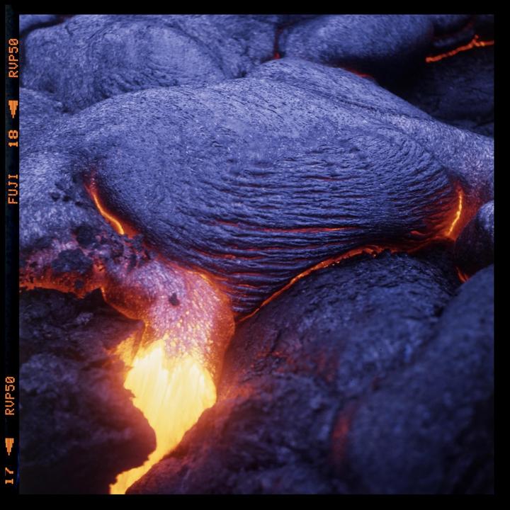 Molten lava flows through dark, cooled volcanic rock.