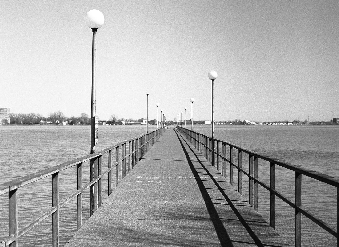 A long pier with lampposts extends into a body of water under a clear sky.