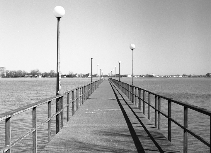 A long pier with lampposts extends into a body of water under a clear sky.