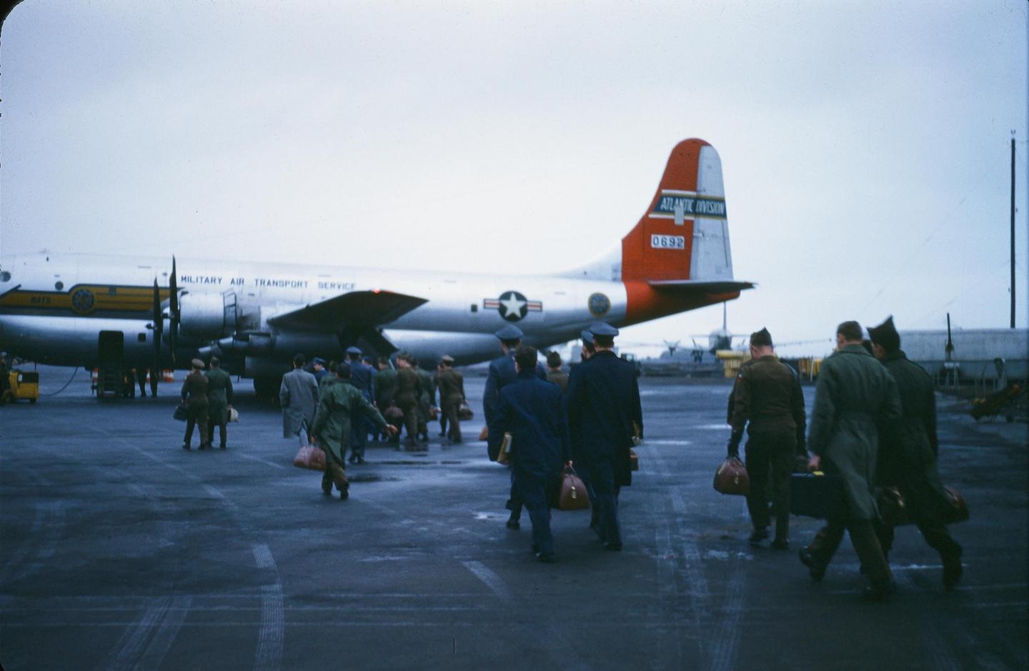 A group of men walk across an airfield toward a large propeller airplane.