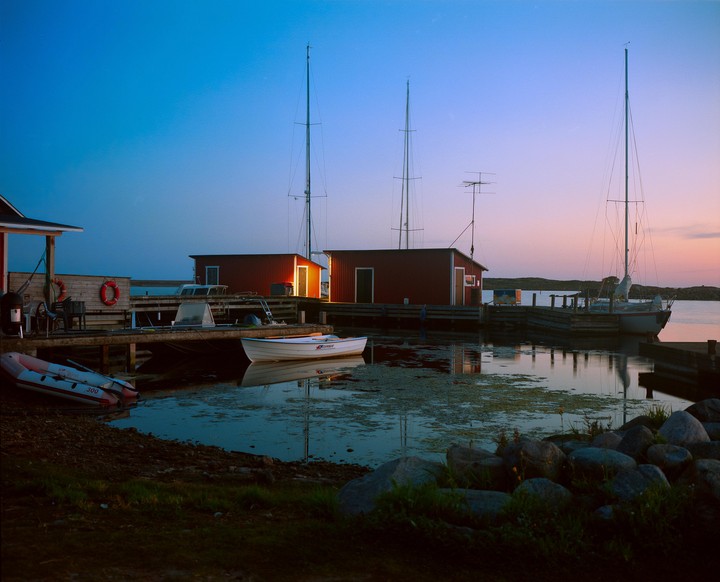 A small harbor with boats and red buildings is visible at dusk.
