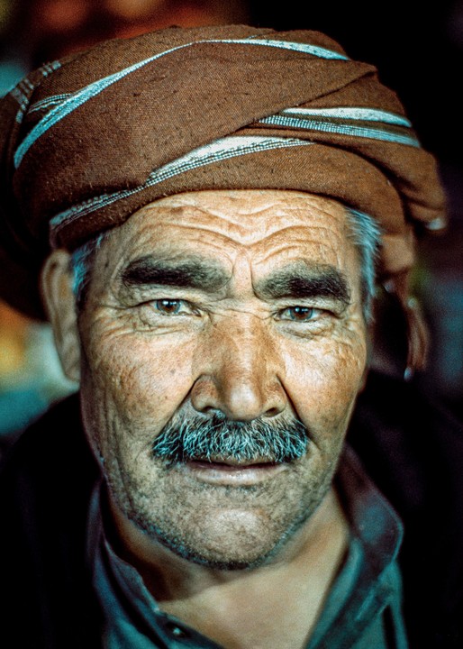 A man with a mustache and a brown turban looks directly at the viewer.