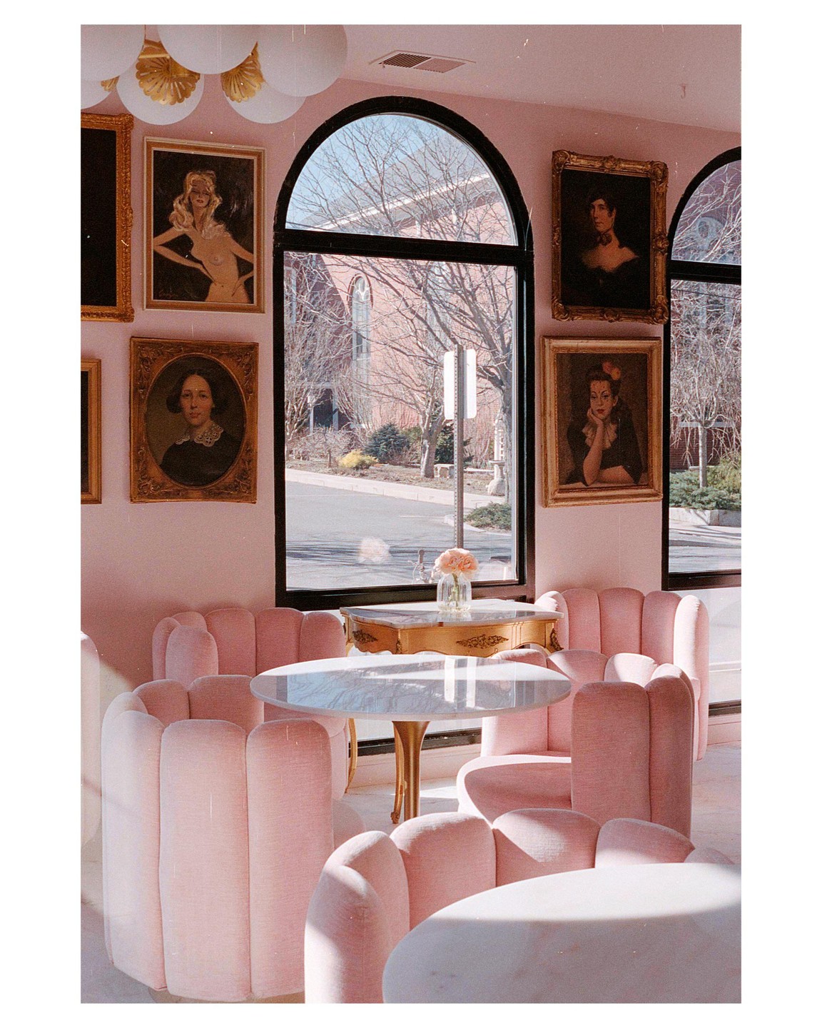 A cafe with pink chairs and tables is visible through an arched window, with paintings on the wall.