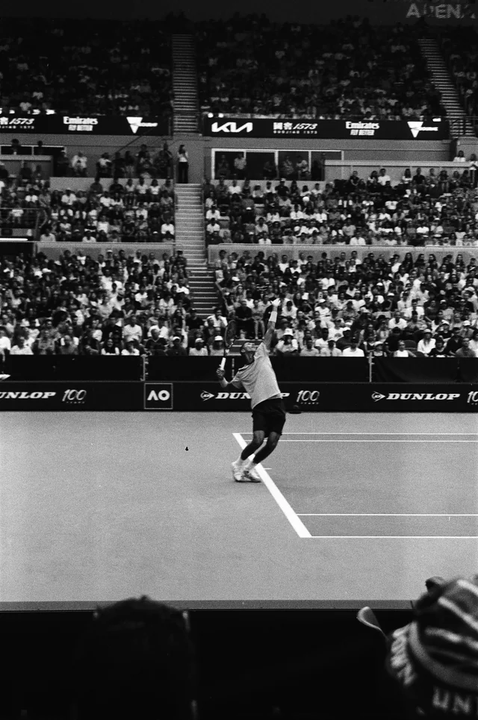 A tennis player serves on a court in a stadium filled with spectators.