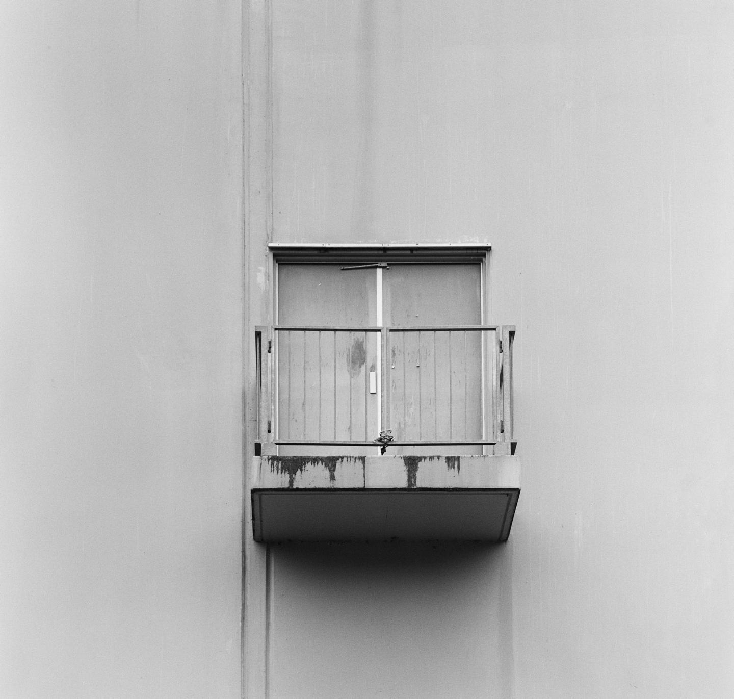 A small balcony with a sliding glass door is centered on a plain building facade.