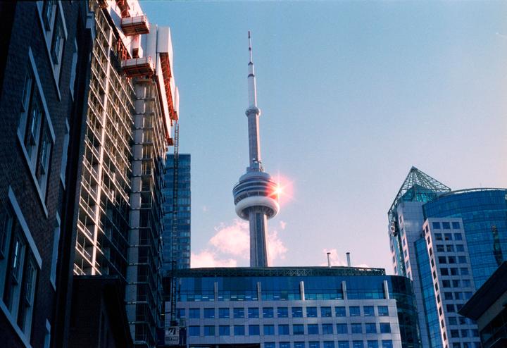 The CN Tower rises above surrounding buildings, with a bright sun flare visible near its observation deck.