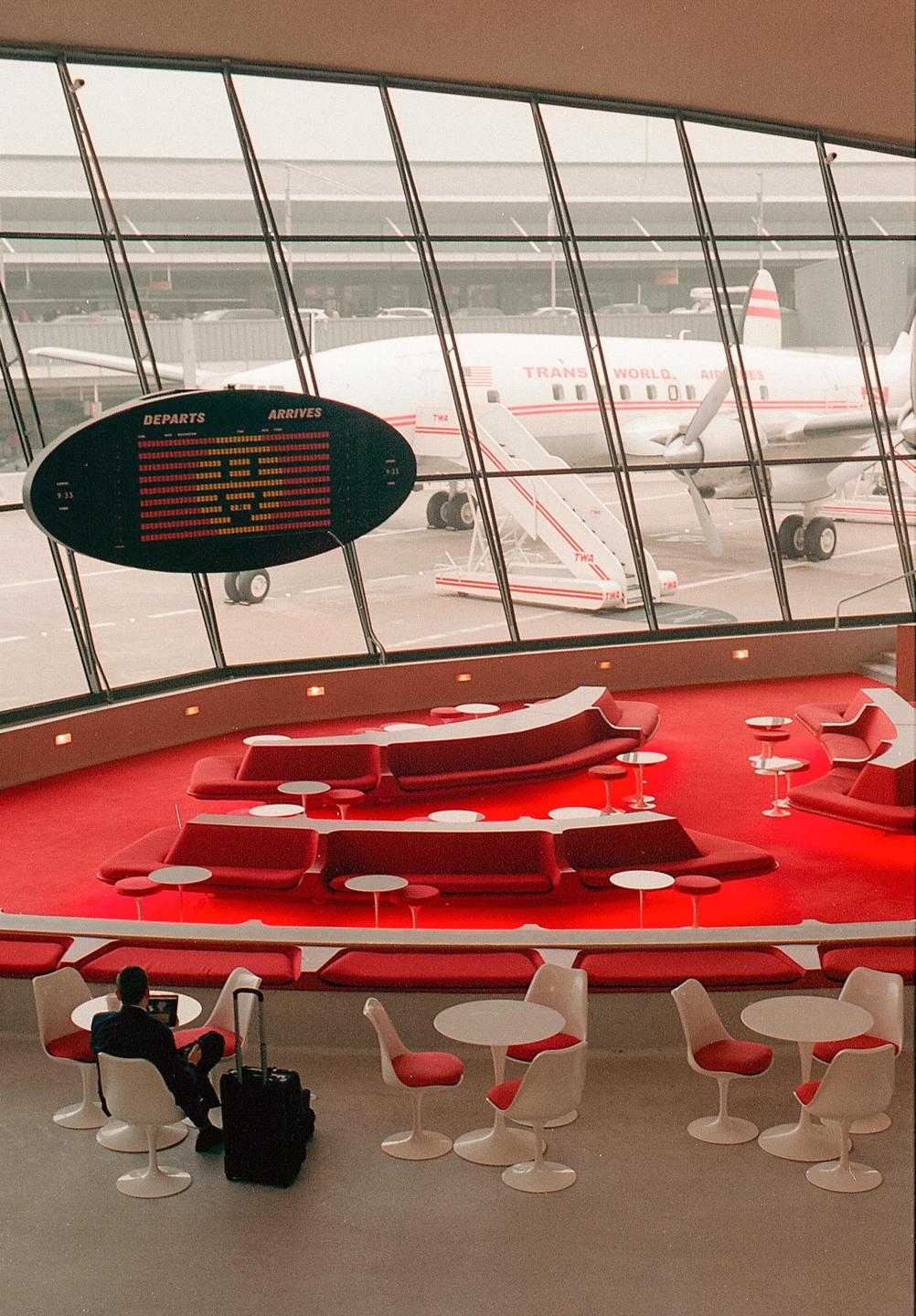 A man sits at a table in an airport lounge with a plane visible through the window.