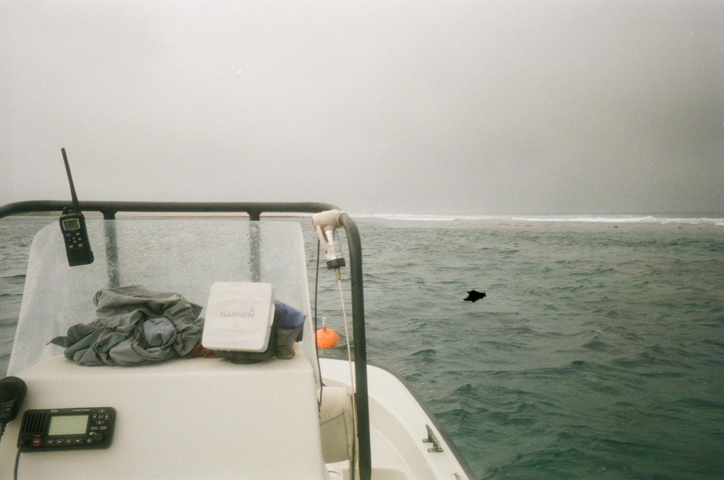 A boat is on the water with a dark shape floating in the distance and a hazy sky.