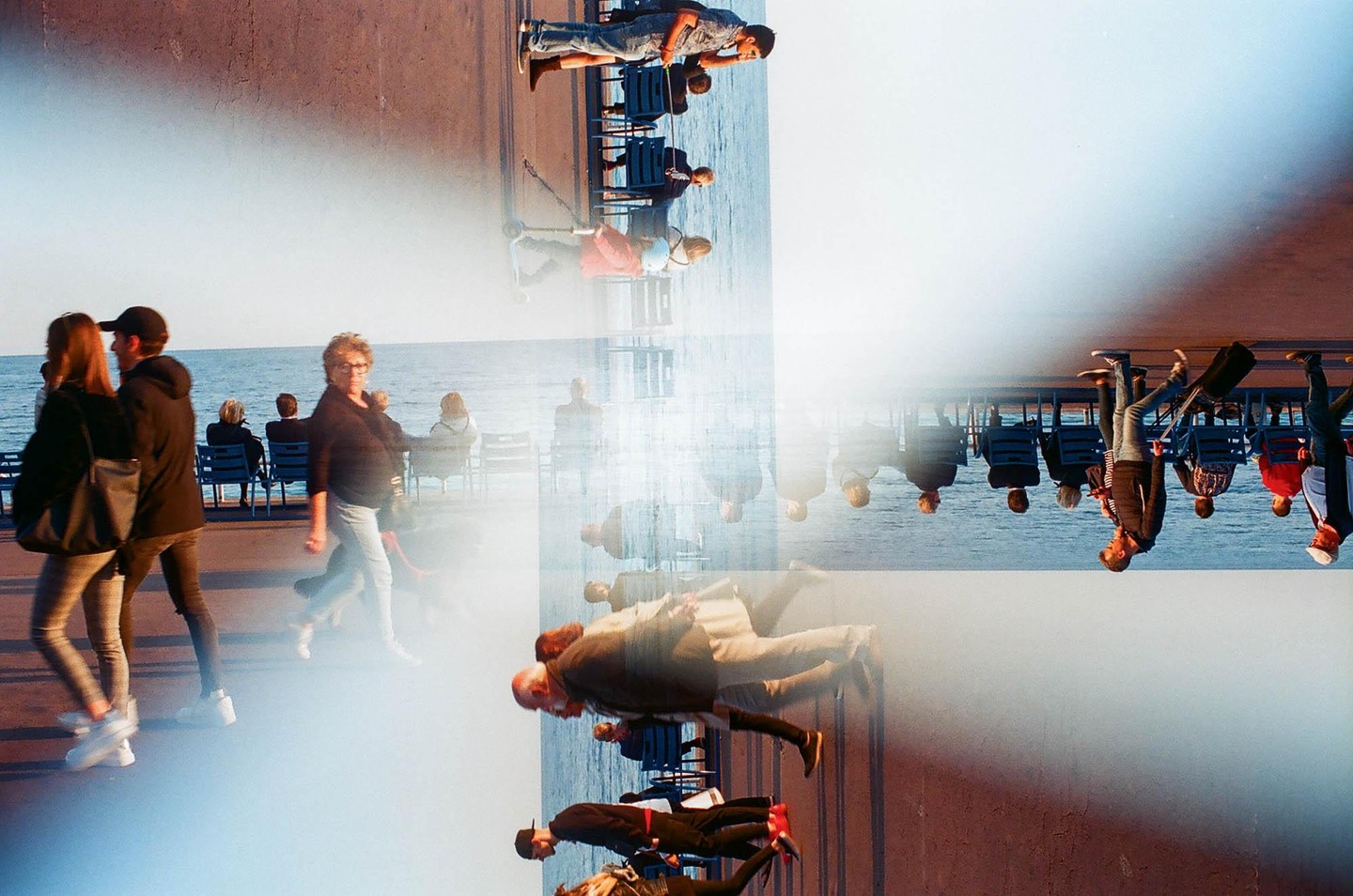A multiple exposure shows people walking and sitting by the sea, with some figures appearing upside down and others right side up.