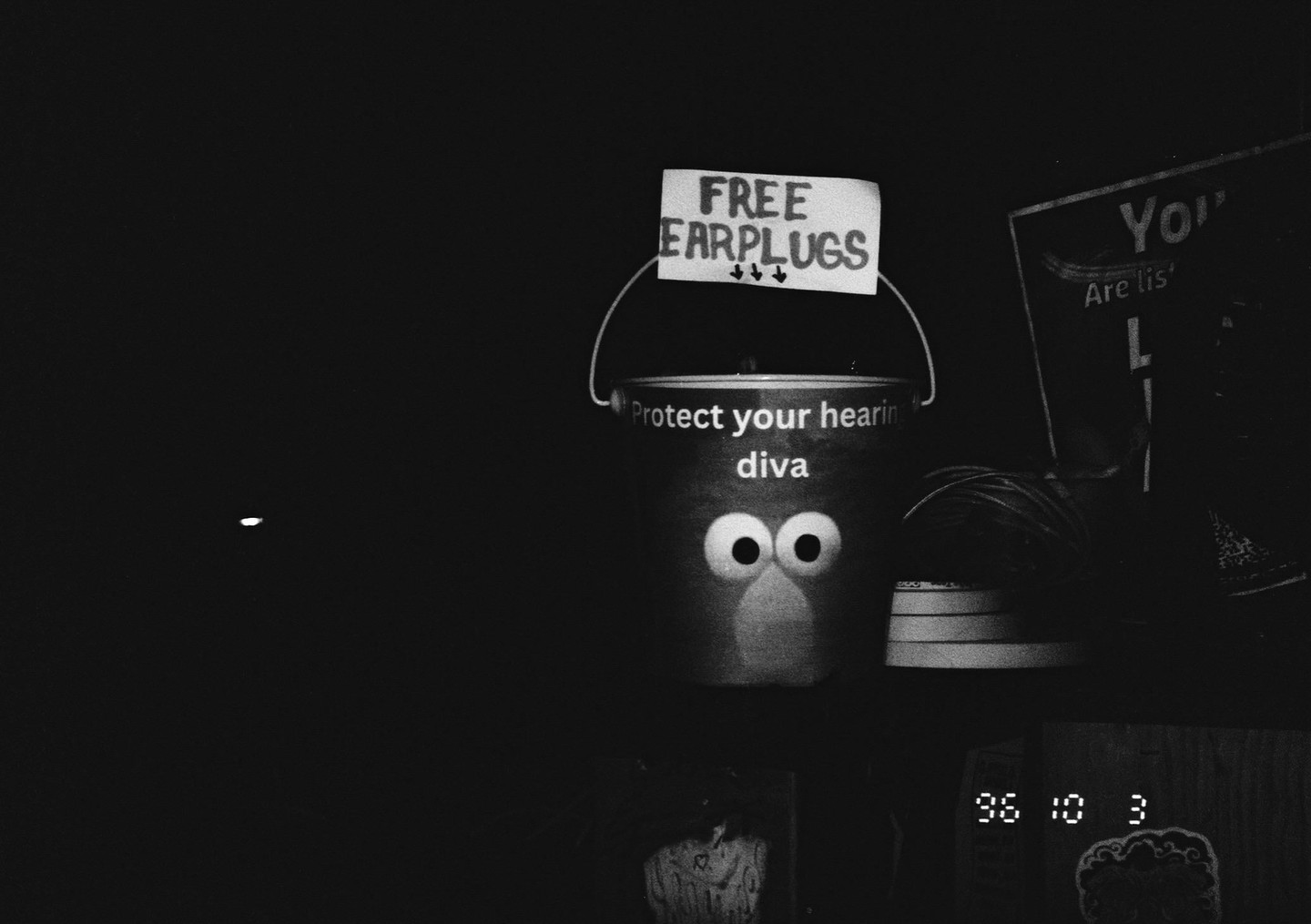 A bucket with googly eyes and a beak is labeled "Protect your hearing diva" and has a sign above it that reads "FREE EARPLUGS."