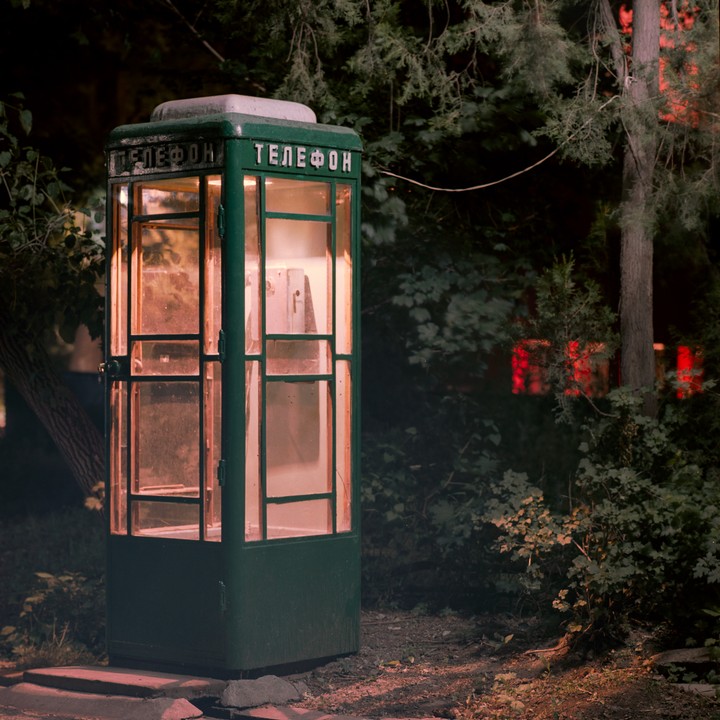 A green telephone booth with glowing windows stands among trees at night.