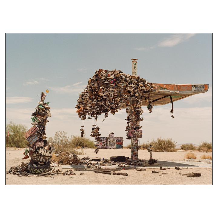A desert landscape features a shoe tree and a shoe station made from an old gas station canopy, both covered in shoes.