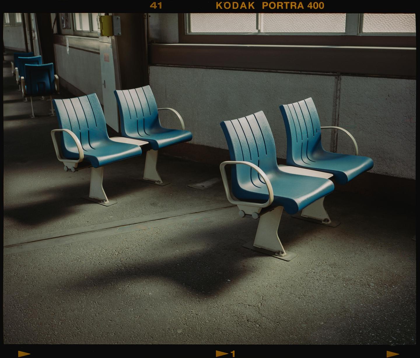 Four blue chairs are arranged in a waiting area with light coming from a window.