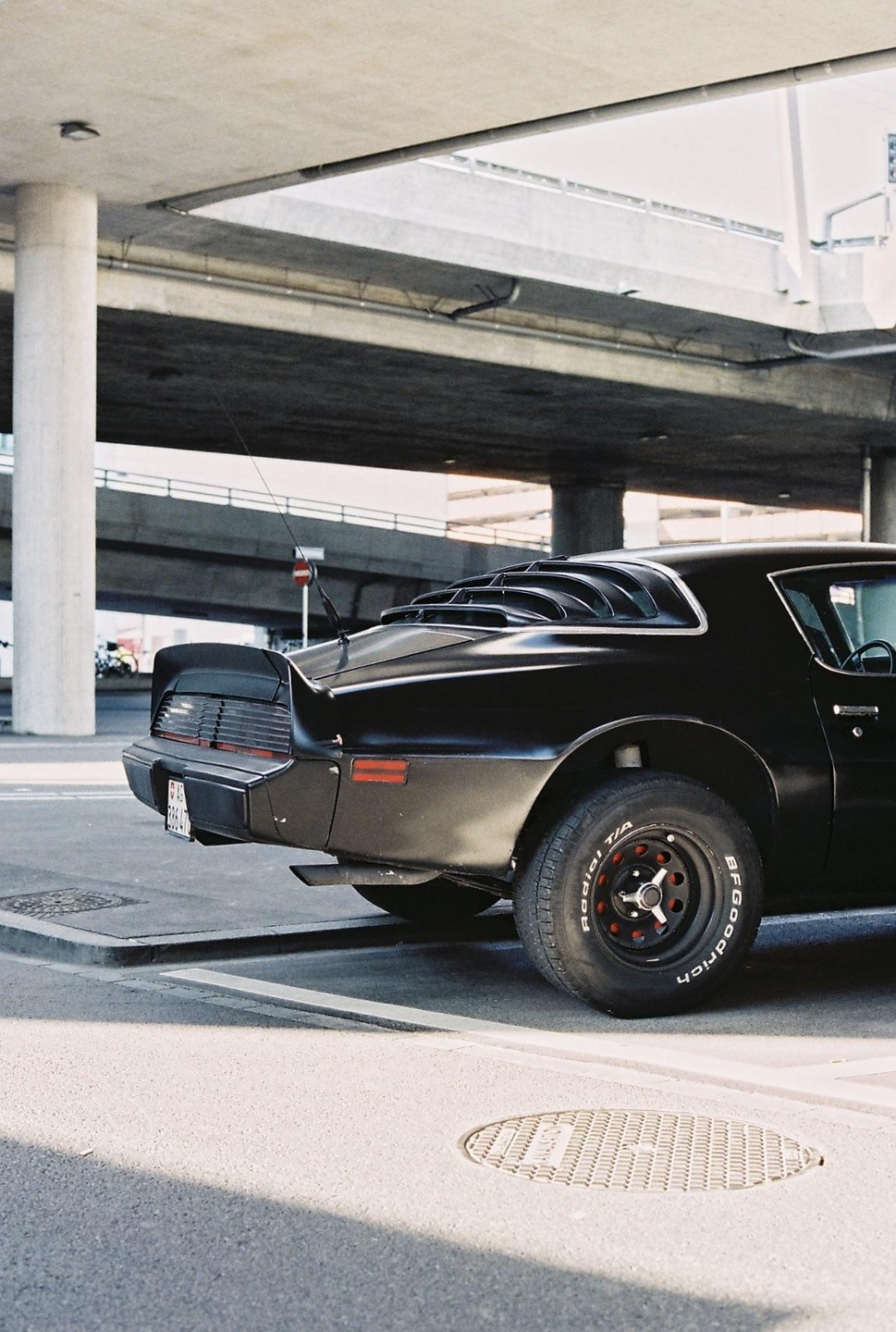 A black car is parked under a concrete overpass.