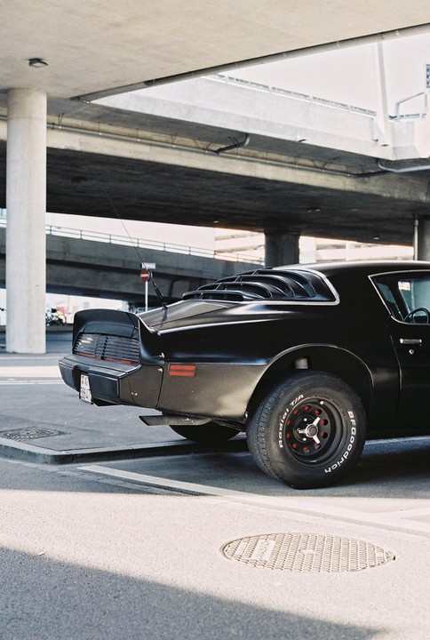 A black car is parked under a concrete overpass.