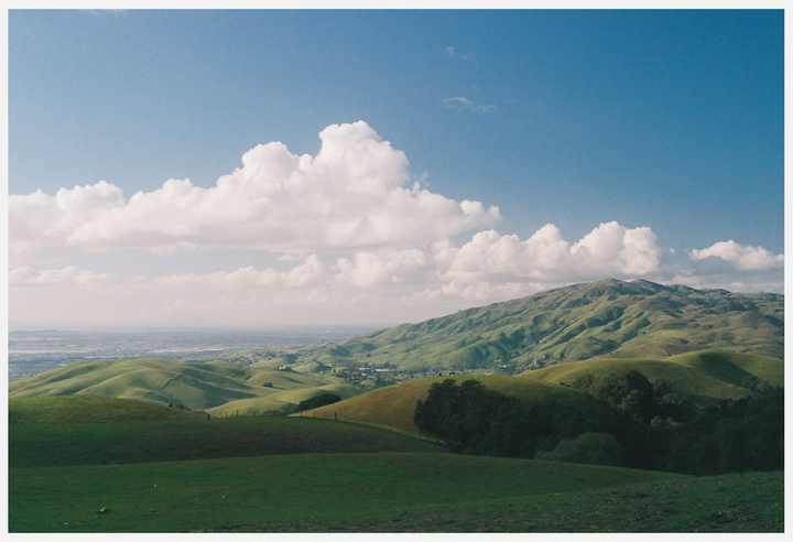 Rolling green hills are visible under a blue sky with white clouds.