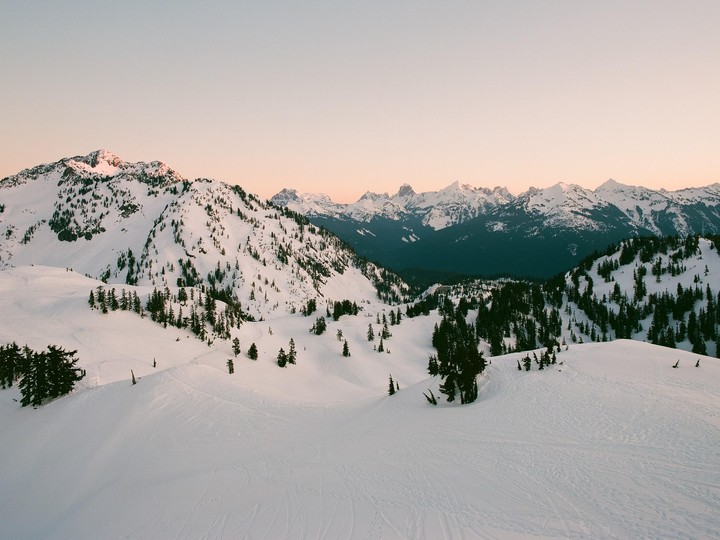 Snow-covered mountains with evergreen trees are visible under a pale sky.