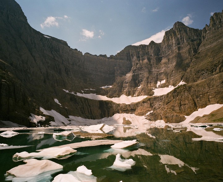 Icebergs float on a lake surrounded by mountains with patches of snow.