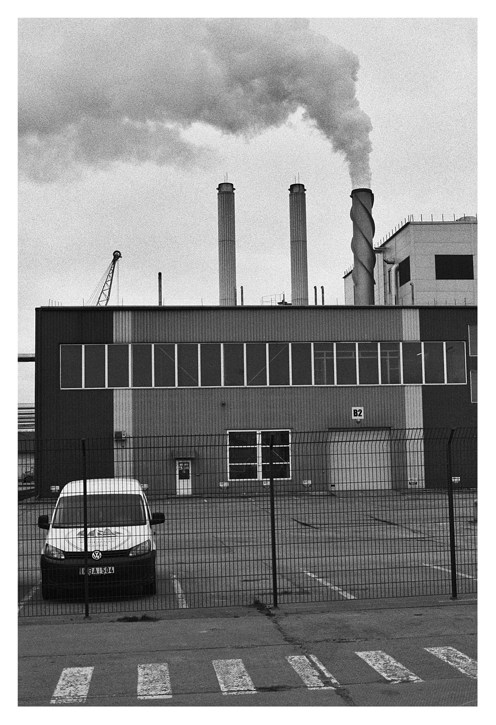 A white van is parked in front of a factory with smoking chimneys.