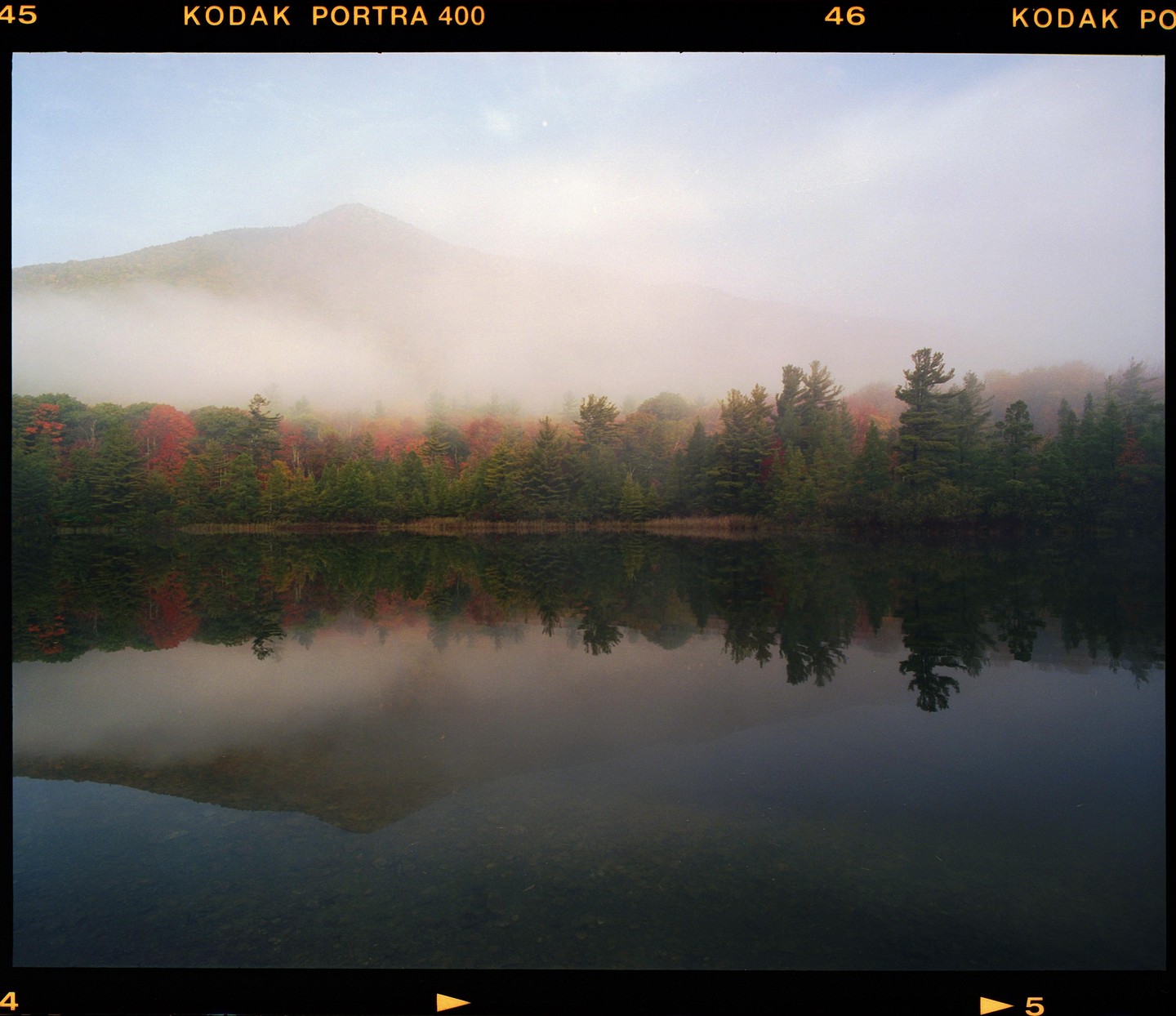 A foggy mountain rises above a lake reflecting autumn trees.