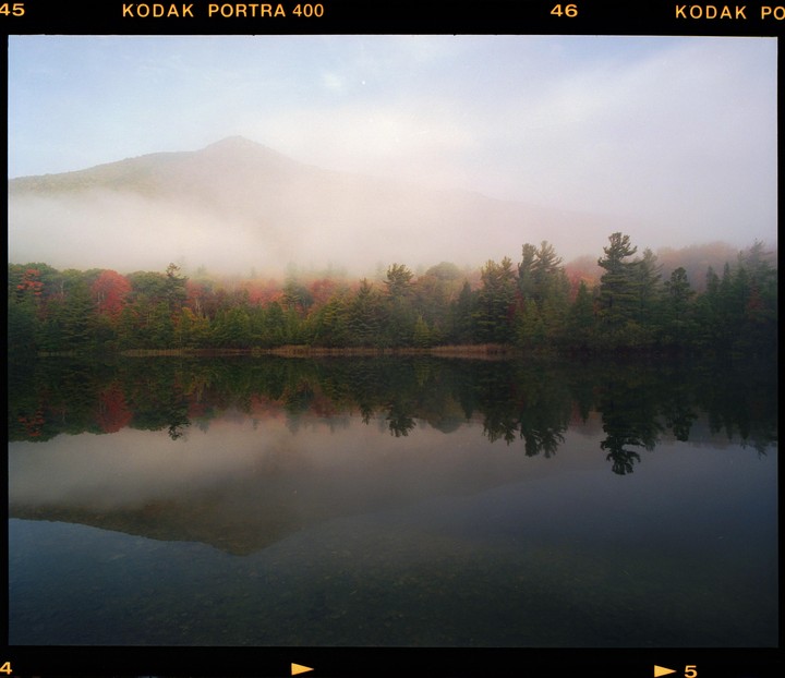 A foggy mountain rises above a lake reflecting autumn trees.