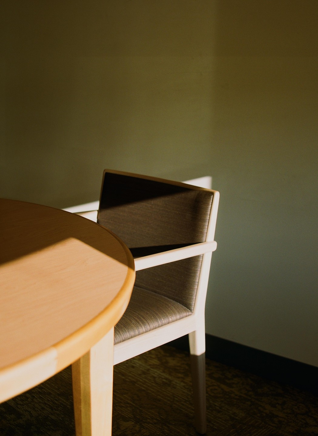 Sunlight illuminates a wooden table and chair in a room with a green wall.