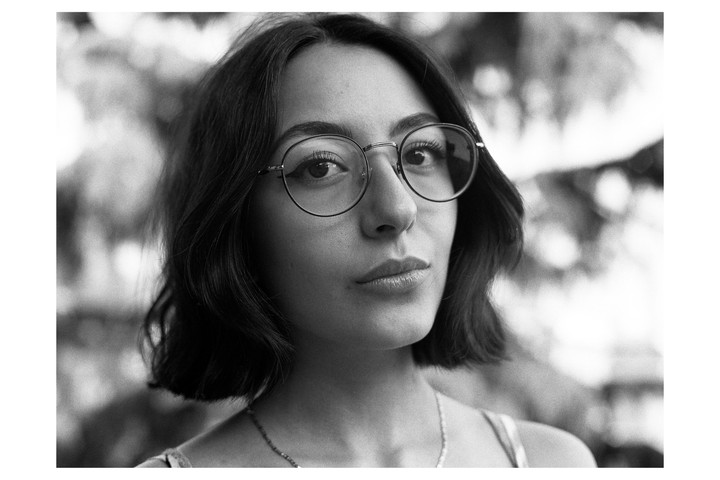 A woman with short hair and glasses looks directly at the viewer.
