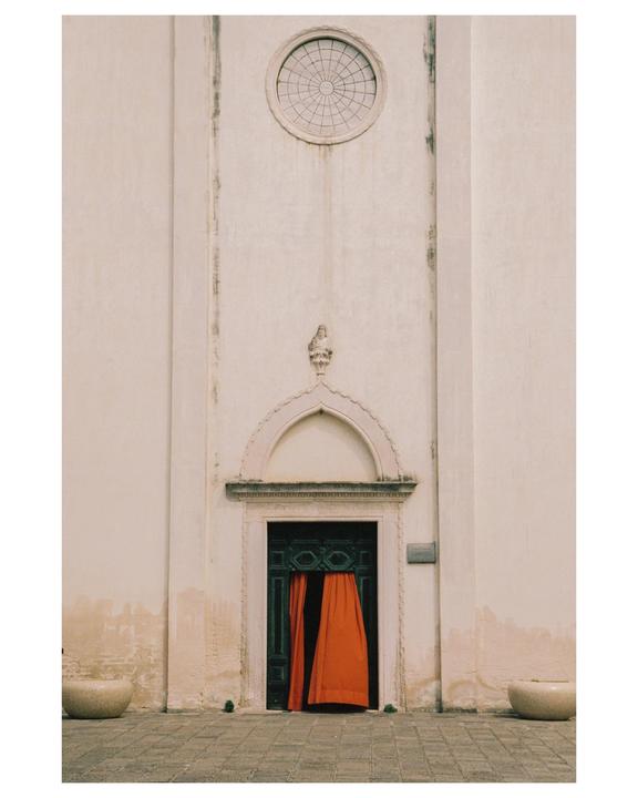 A building with a dark green door and bright orange curtains is visible from a low angle.