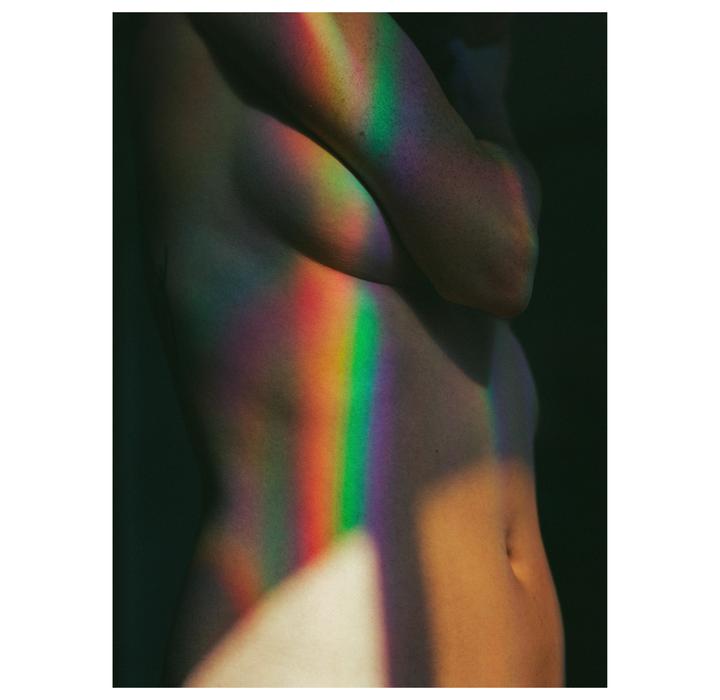 A rainbow light pattern is cast across the torso and arm of a person.