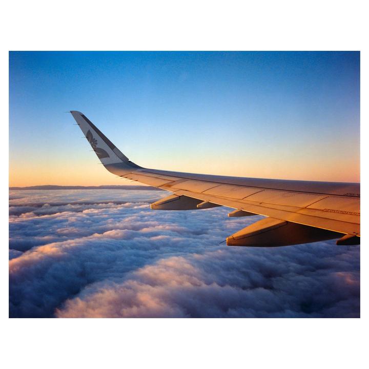 An airplane wing is visible above a sea of clouds during sunset.