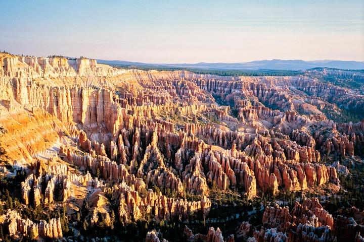 An aerial landscape view shows the vast, intricate rock formations of Bryce Canyon National Park under a clear sky.