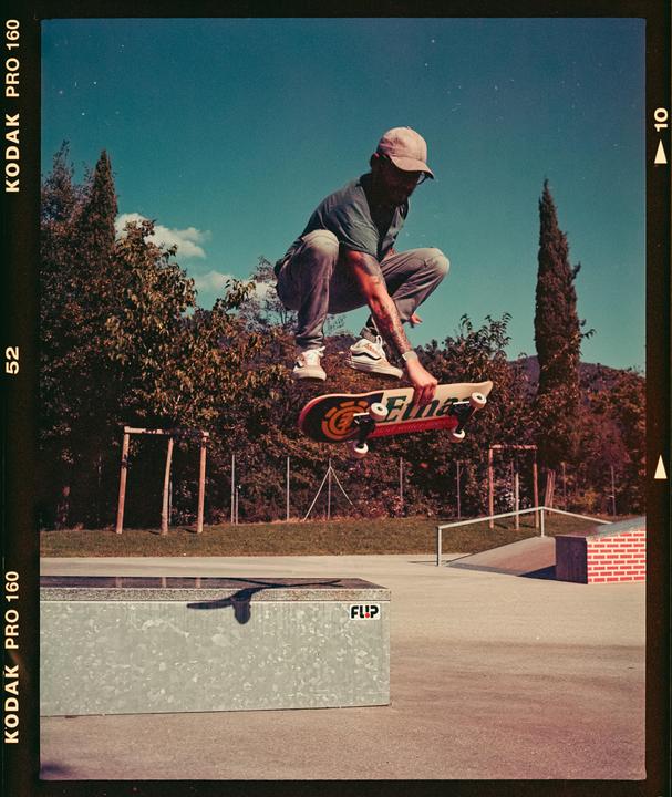 A man in a cap is captured mid-air on a skateboard at a skatepark.