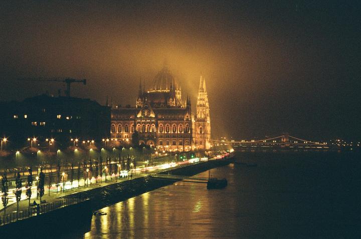 The Hungarian Parliament Building is illuminated at night, with a bridge and river in the foreground.