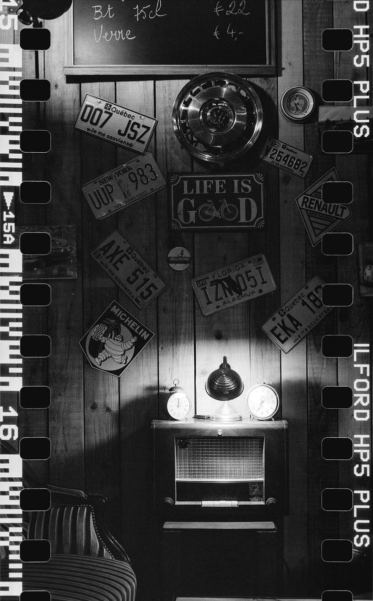A collection of license plates and signs are displayed on a wooden wall above a radio and two alarm clocks.