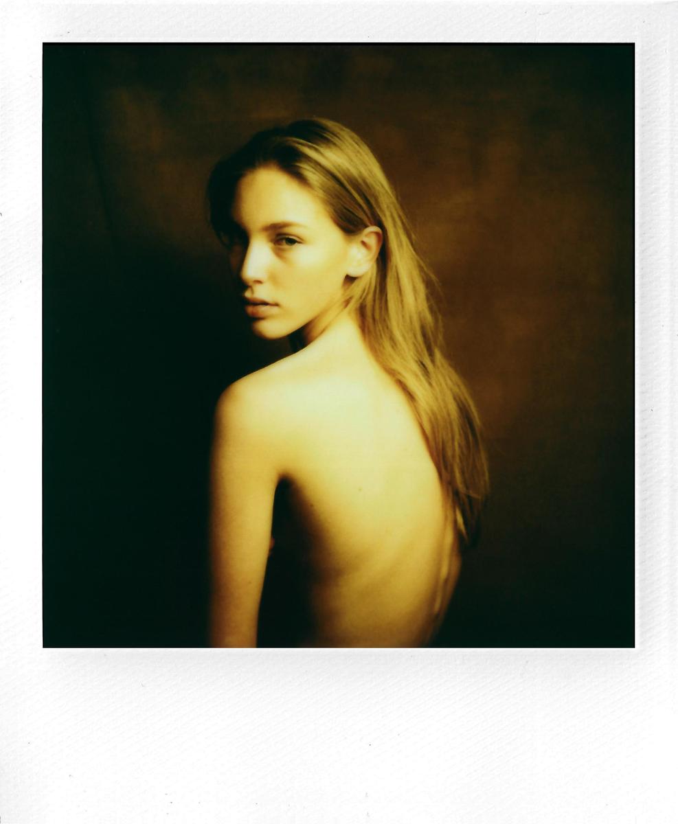 A woman with long hair looks over her shoulder at the viewer.