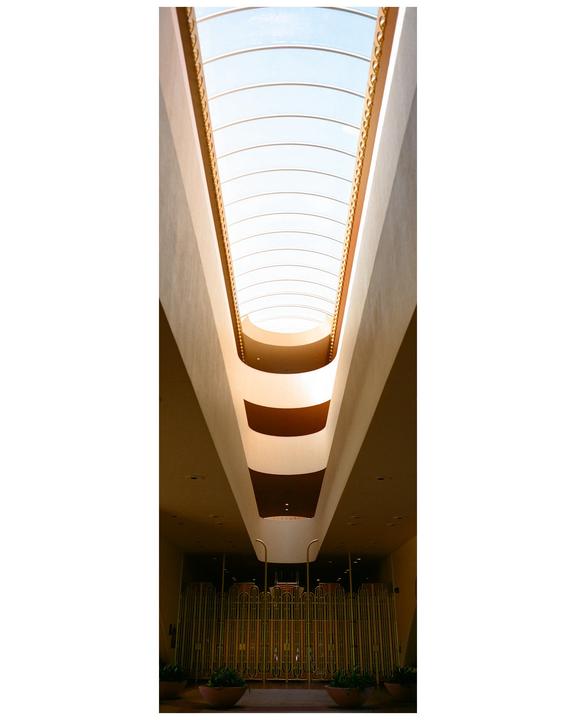 A long, narrow skylight illuminates the interior of a building with a golden gate at the bottom.