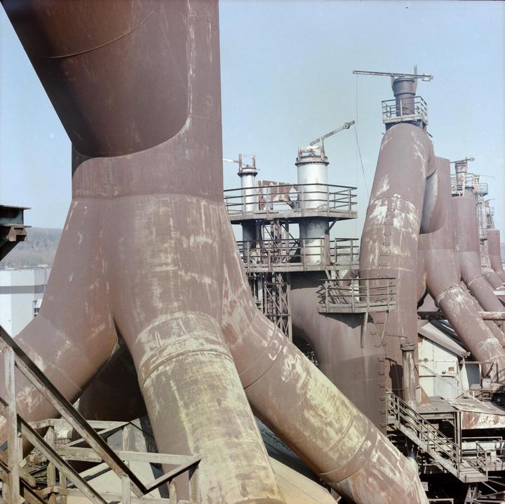 A large industrial structure with multiple rusty pipes and platforms is shown under a clear sky.