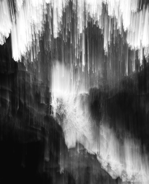 A black and white abstract image shows vertical streaks of light against a dark background.