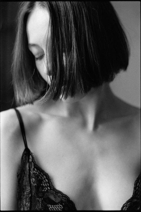 A woman with short hair and a lace top looks down, with her face partially obscured by her hair.